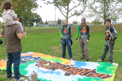 Three people stand talking near a banner laid on the grass.