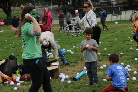 A woman with green zombie face paint throws a ball during the lawn game.