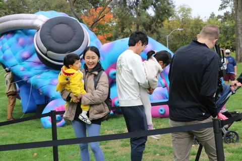 A family stands near a large inflatable caterpillar sculpture in the park.