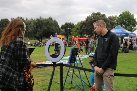 A man stands near a camera rig in a wide festival field.