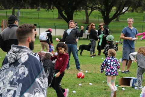 Two men stand among scattered balls as a dog looks on.