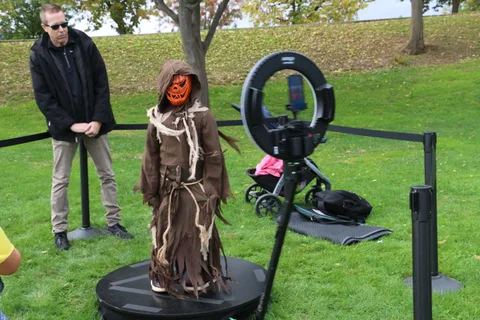 A man watches a child in a scarecrow costume use the 360 photo booth.