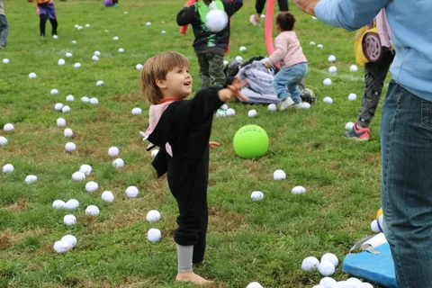 A girl in a black costume reaches up for a green balloon.