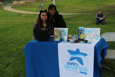 Two women smile from behind a Swim America table at the festival.