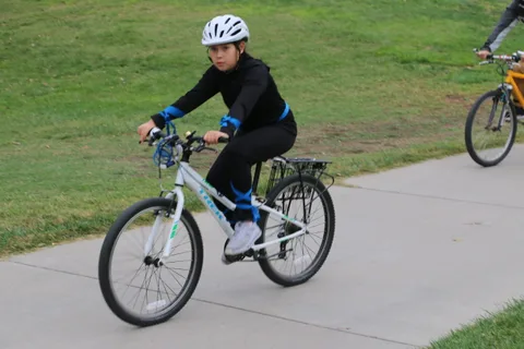 A woman in black rides alone on a white bike against a hillside.