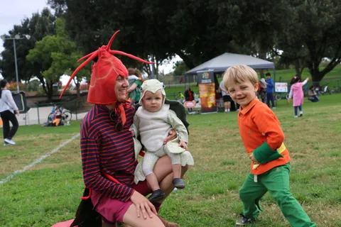 A toddler in a lamb costume reaches toward her brother in orange.