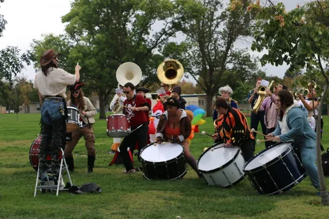 A brass player performs standing on a stool above the drum corps.