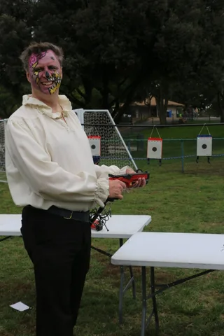 A person aims a red toy blaster down an outdoor shooting range.