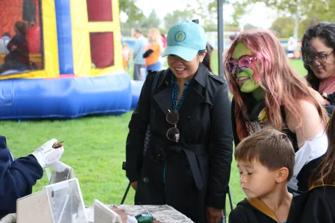 A woman smiles next to a child in a black robe costume.