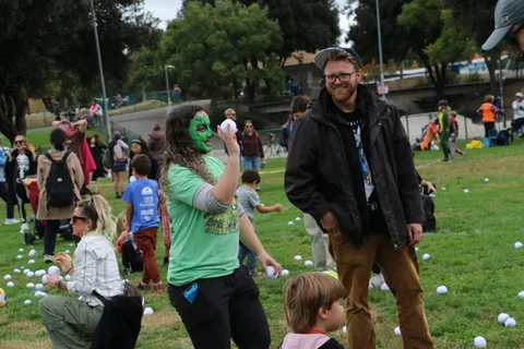 A woman with green face paint reaches during the lawn ball game.