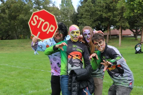 A man and two women in skull makeup pose together holding a stop sign.