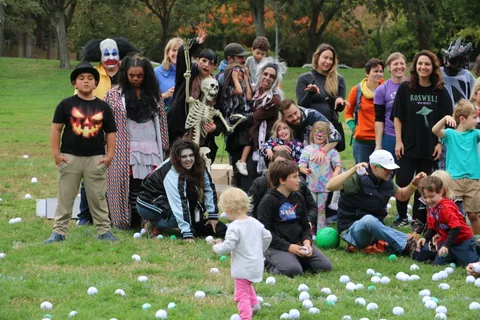 A group in colorful costumes including a clown and a skeleton pose together with a toddler.