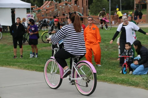 A woman rides a pink cruiser bike past costumed prisoners in the background.