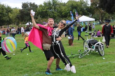 A man in a skeleton costume and cape cheers as a colorful ball flies overhead.
