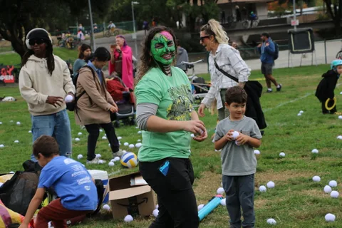 A woman with green face paint smiles while holding a ball near a boy.