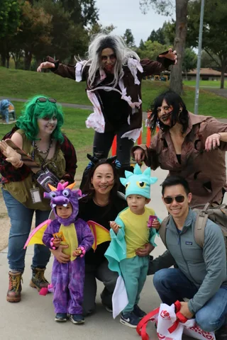 A family smiles together, with two children dressed as a dragon and a dinosaur.