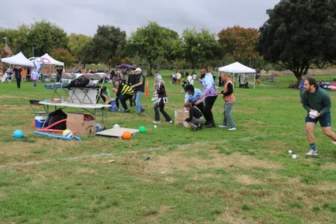 Kids gather near equipment boxes and a blue tarp on the grass.