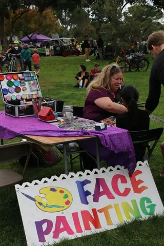 A rainbow-lettered face painting sign sits near the booth tables.