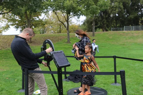 A girl in a butterfly costume dances beside a man aiming at a target.
