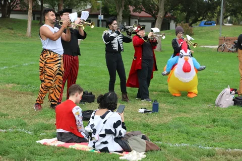 Trumpet players in tiger and skeleton print pants perform beside an inflatable chicken.