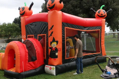 An orange and black pumpkin-themed inflatable bounce house stands empty in the park.