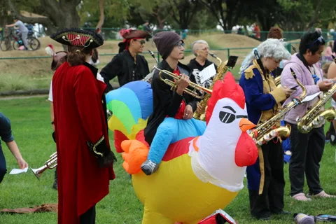 A costumed group including an inflatable rooster gathers on the grass.