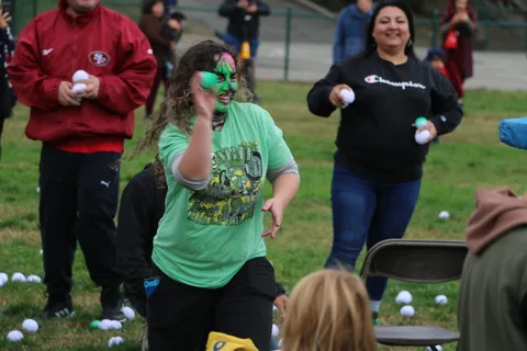 Two adults playfully toss white balls at each other on the grass.