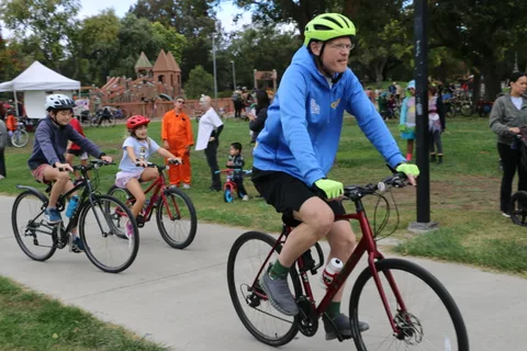 A father and child ride bikes together down the path.
