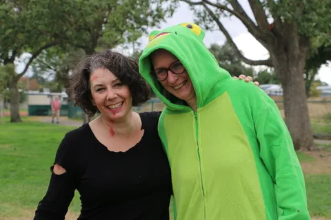 Two women smile together in a park, one in a green costume.