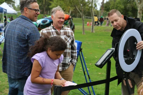 A man and a young girl look up together at the ring-light photo booth.