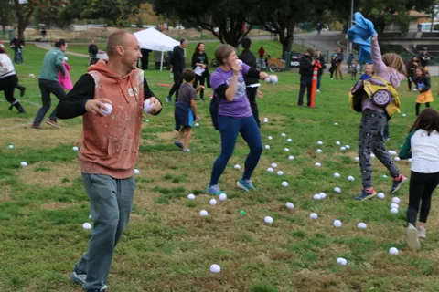A man in a vest throws a ball as a teen looks on amid scattered balls.