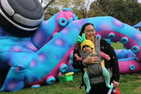 A woman holds a costumed baby near the giant inflatable tentacle attraction.