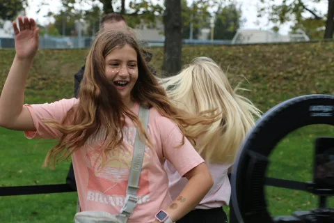 Two girls flip their hair and laugh in front of the ring-light photo booth.
