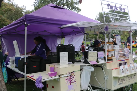 Two people work at a purple-canopy vendor booth.