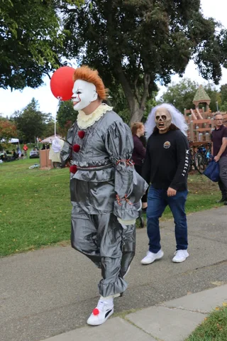 A person in a Pennywise-style clown costume holds a red balloon near another masked figure.