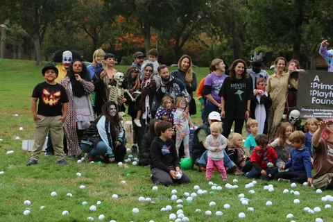 A group of costumed participants gathers for a photo with children seated in front.
