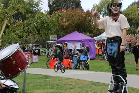 A man in cowboy hat and skeleton face paint stands near parked bikes and a purple tent.