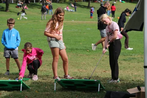 Two girls play a golf-toss cornhole game together in the park.