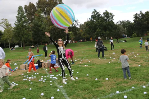 A girl in a skeleton costume jumps in the air as a colorful ball flies overhead.
