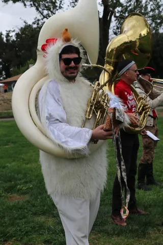 A musician wears a white flower headdress and sunglasses while playing a sousaphone.