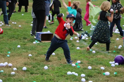 A boy in a red shirt shouts mid-throw amid colorful boxes on the grass.
