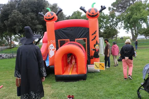 A hooded grim reaper figure walks past an orange pumpkin-themed inflatable slide.