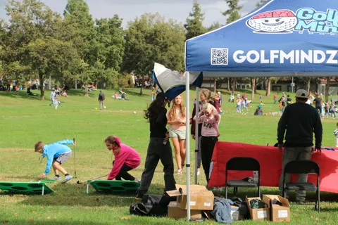 Children and adults gather at a GolfMindz booth tent in the park.