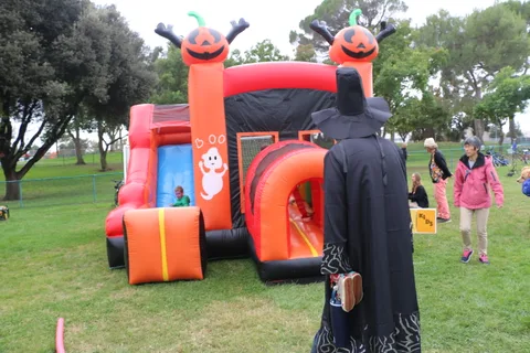 A child plays on an orange pumpkin-themed inflatable slide as a hooded figure walks by.