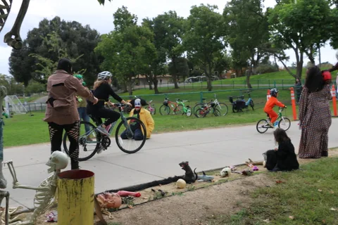 Cyclists ride past cemetery-themed decorations in the park.