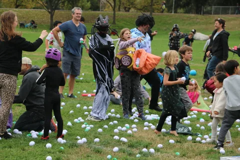 A cluttered group of costumed children and adults gather on a grassy field.