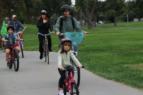 A parent and two children ride bikes together toward the camera.