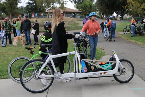 A crowd of riders and a white cargo bike gather at the edge of the park.
