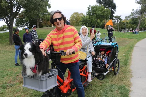 A man with his dog in a bike basket stands among a group of riders.