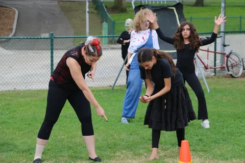 Two performers in black costumes strike dynamic dance poses on the grass.